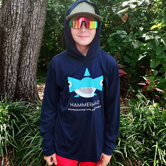 Boy wearing a Navy Hammerhead Hooded Sun Protective Long Sleeve Shirt UPF 50+ by ShapeShifter Fish and Friends, standing outdoors among trees and foliage.