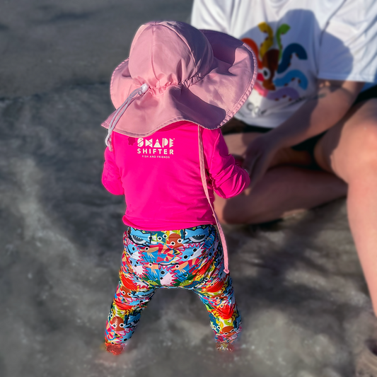 Baby in sun protective UPF swim pants standing on a sandy beach