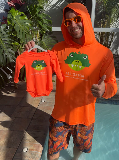 Man wearing a Neon Orange Alligator Hooded Sun Protective Shirt UPF 50+ by ShapeShifter Fish and Friends, holding a matching alligator baby onesie by a pool.