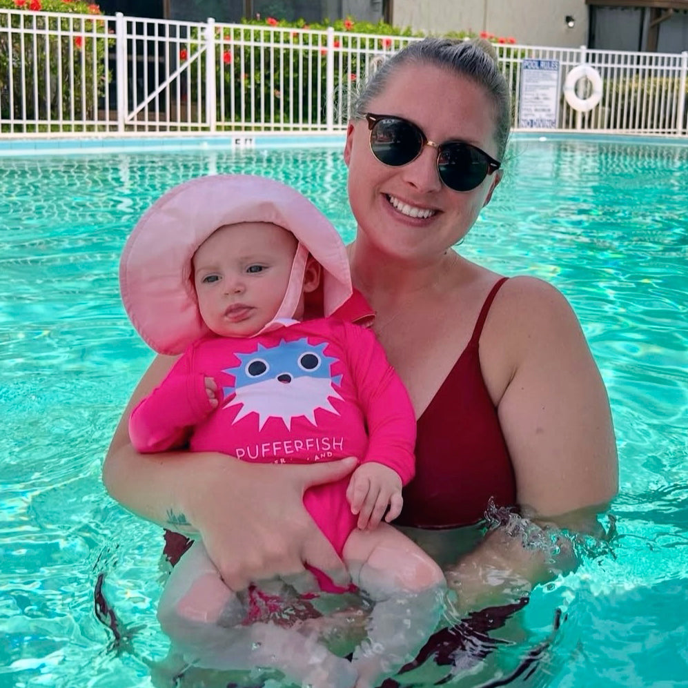 Woman and baby in a pool wearing Hot Pink Pufferfish Upf50 Baby Onesie by ShapeShifter Fish and Friends