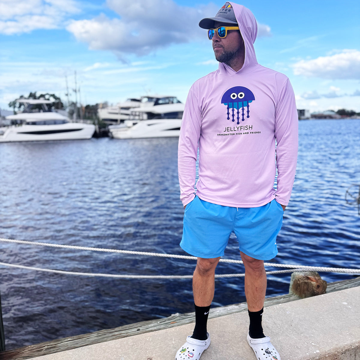 Man wearing a Lilac Jellyfish Hooded Sun Protective Long Sleeve Shirt UPF 50+ by ShapeShifter Fish and Friends by a marina lifetsyle