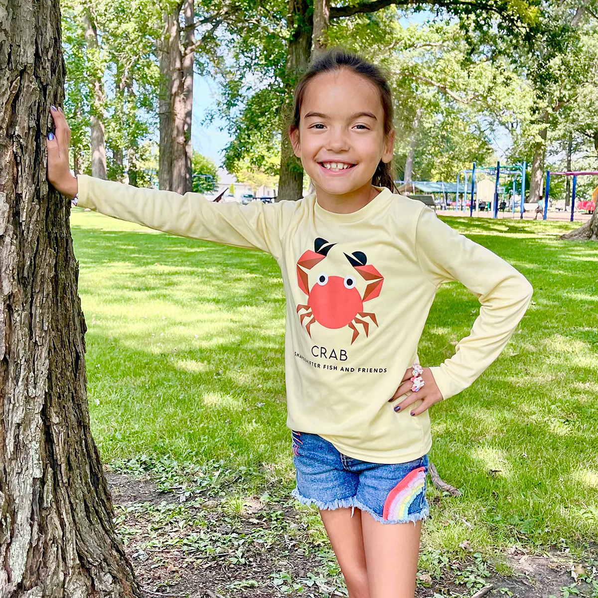 Girl standing by a tree wearing a Yellow Crab Long Sleeve Shirt UPF 50+ sun shirt ShapeShifter Fish and Friends lifestyle