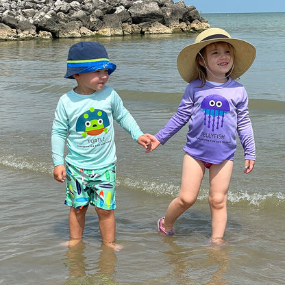two toddlers wearing a Seagrass Turtle and lilac jellyfish UPF 50+ sun wear by ShapeShifter Fish and Friends lifestyle on the beach