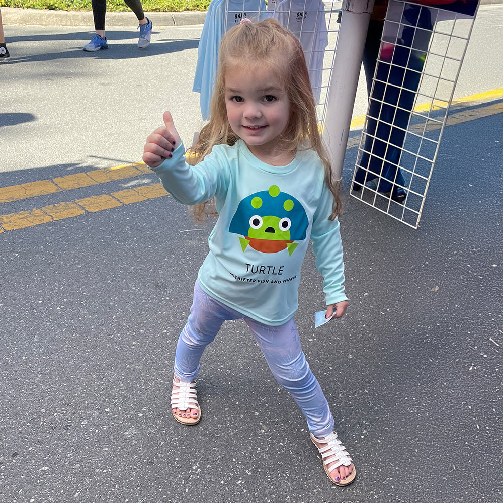 Little girl wearing a Turtle Sun Protection Shirt by ShapeShifter Fish and Friends giving a thumbs up