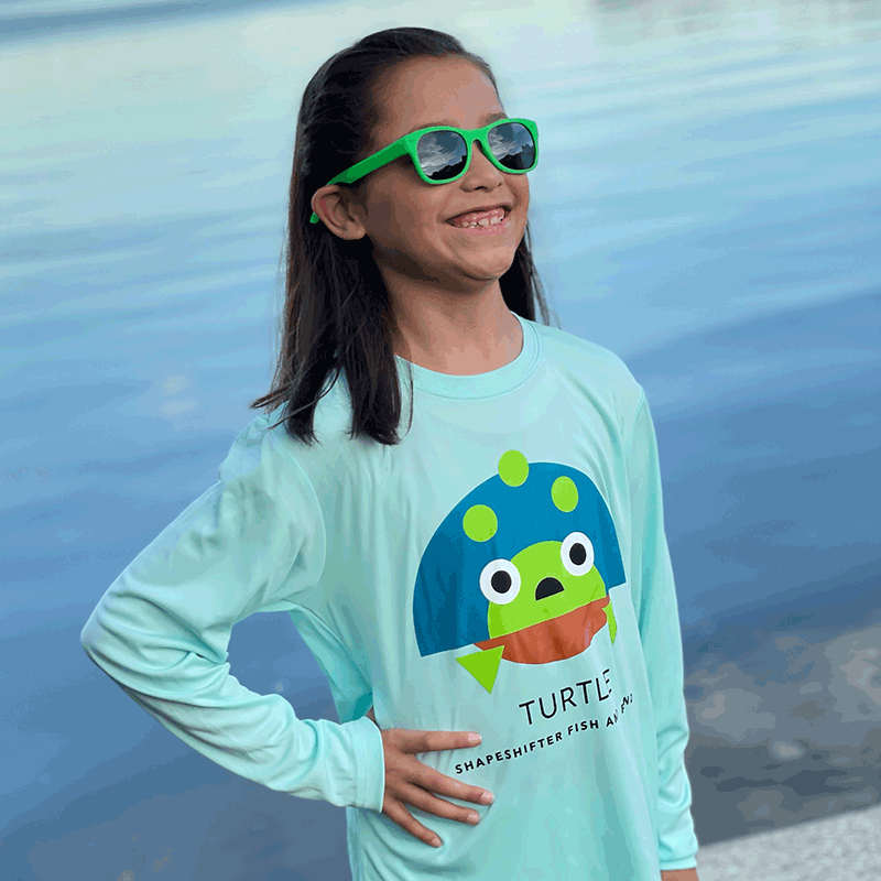 girl wearing a Seagrass Turtle Upf50 Sun Protection Shirt and unbreakable sunglasses by ShapeShifter Fish and Friends standing by the water