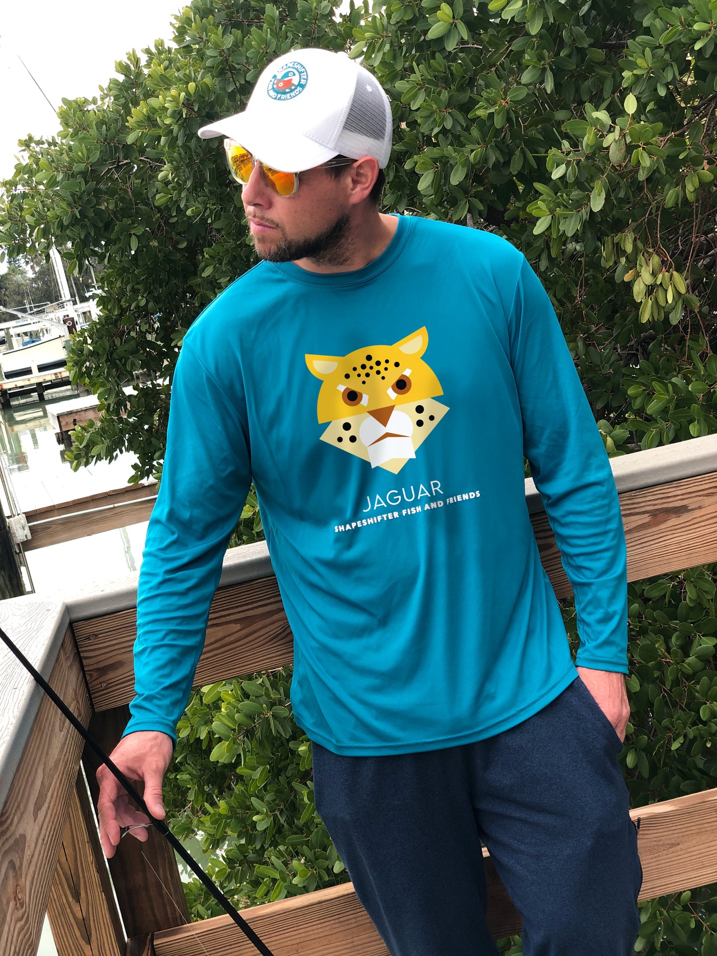 Man wearing a teal long-sleeve UPFshirt with a jaguar graphic and text, standing outdoors.