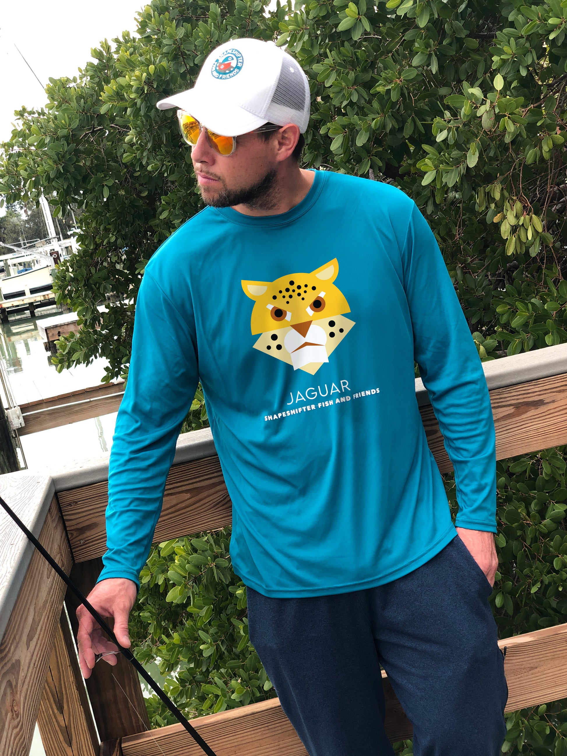 Man wearing a teal long-sleeve UPFshirt with a jaguar graphic and text, standing outdoors.