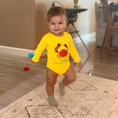 Child wearing a UPF 50+ crab onesie sunwear by ShapeShifter Fish and Friends, standing on a patterned rug