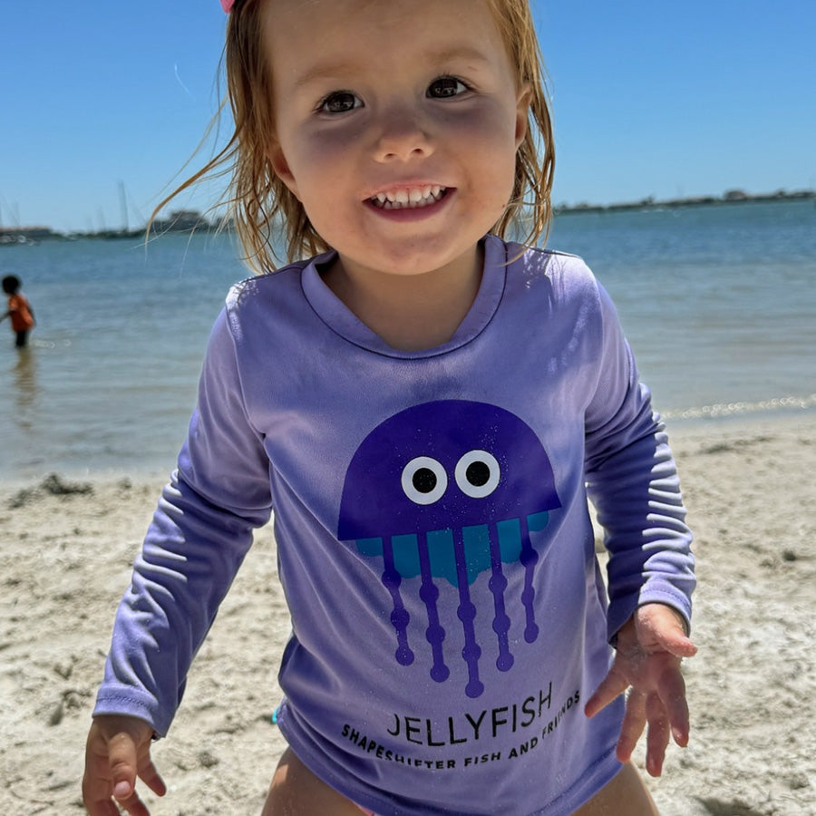 Toddler on the beach wearing a purple Jellyfish  Long Sleeve UPF 50+ sun shirt by ShapeShifter Fish and Friends lifestyle