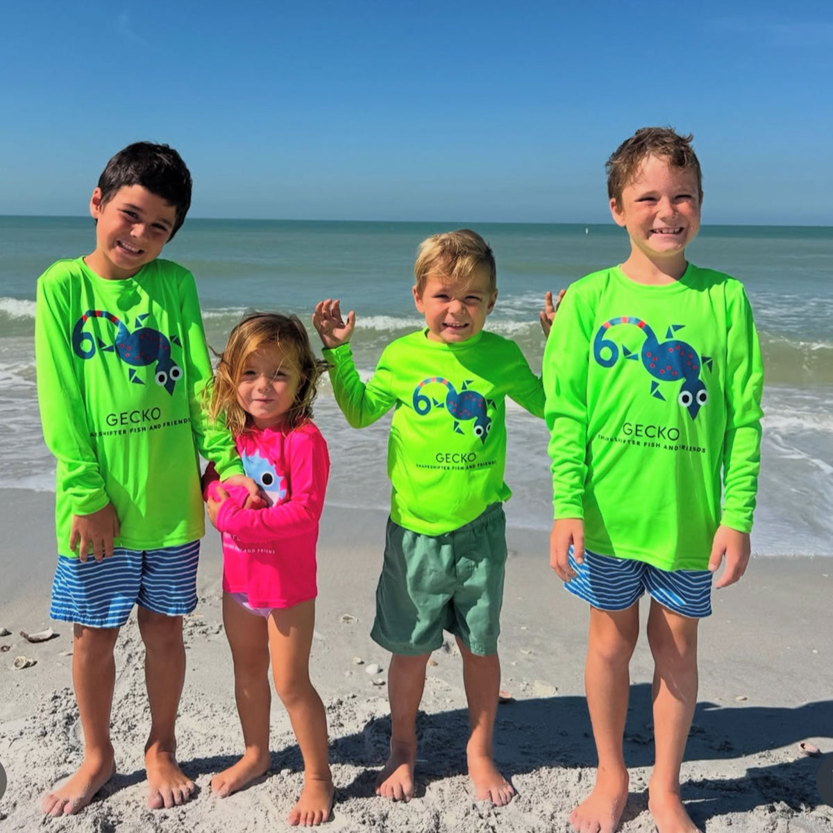 Four children in swim-safe colors wearing high visibility Gecko Upf50 Sun Protective Long Sleeve Shirt UPF 50+ by ShapeShifter Fish and Friends on the beach lifestyle