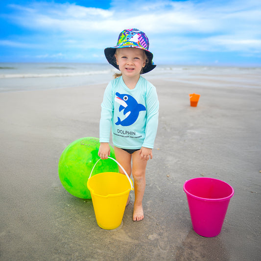 Toddler on the beach wearing a Dolphin Upf50 Sun Protective Long Sleeve Shirt and reversible bucket hat by ShapeShifter Fish and Friends lifestyle