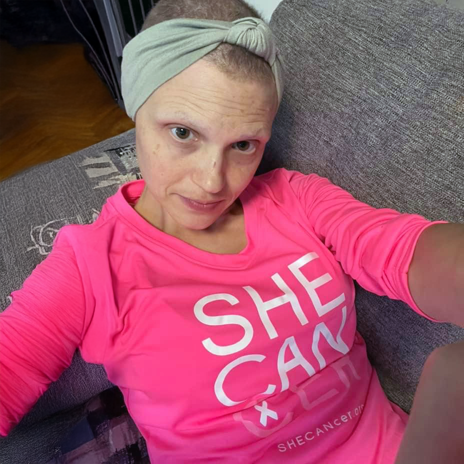 Woman wearing a Shecancer Hot Pink Ladies V Neck by ShapeShifter Fish and Friends, sitting on a couch.