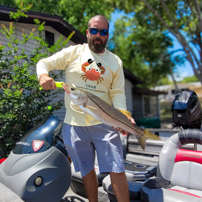 Man holding a large fish next to a boat, wearing a Canary Yellow Crab UPF 50+ sun shirt by ShapeShifter Fish and Friends
