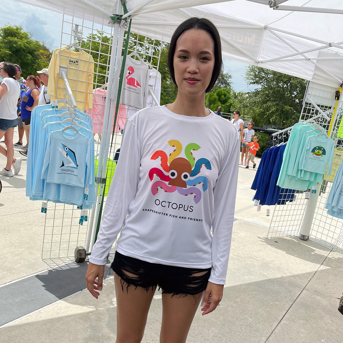 Woman wearing a White Rainbow Octopus Sun Protective Long Sleeve Shirt UPF 50+ sunwear by ShapeShifter Fish and Friends at an outdoor market.
